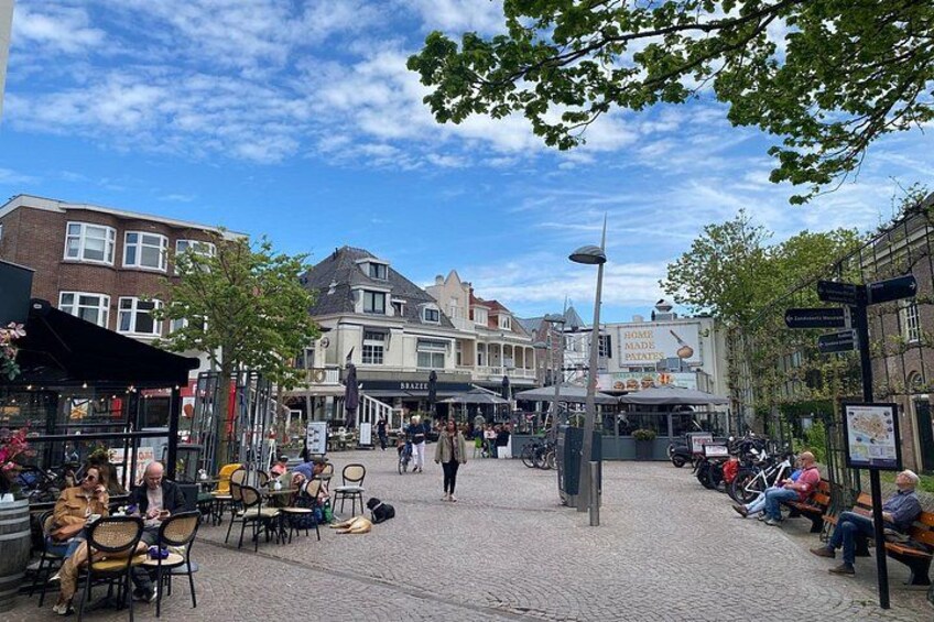 Ein Kopfsteinpflasterplatz mit Außenbestuhlung, Fußgängern und historischen Gebäuden. 3