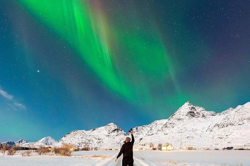 Een persoon staat in een besneeuwd landschap met bergen op de achtergrond en het Noorderlicht aan de hemel. 3