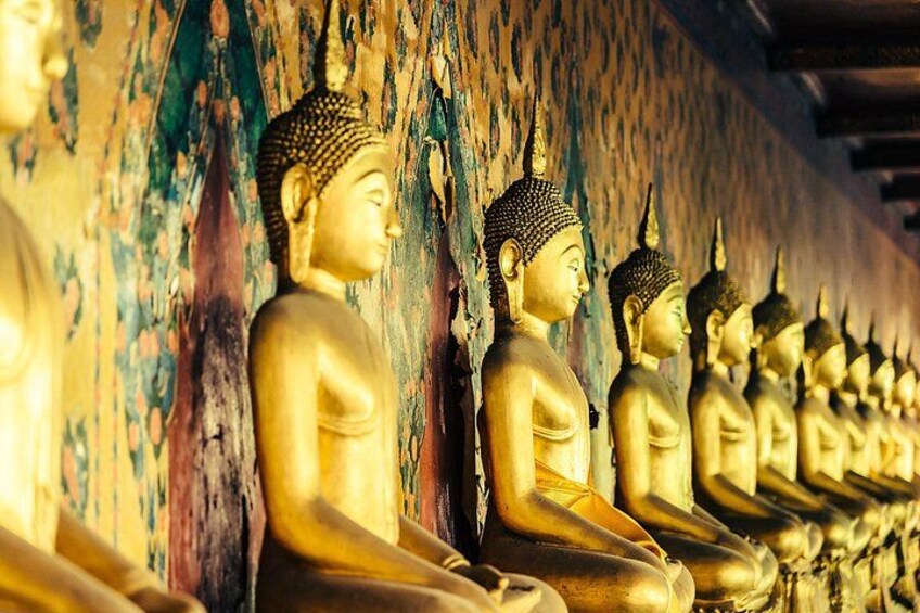 Eine Reihe goldener Buddha-Statuen vor einer Wand mit abblätternder Farbe. 3