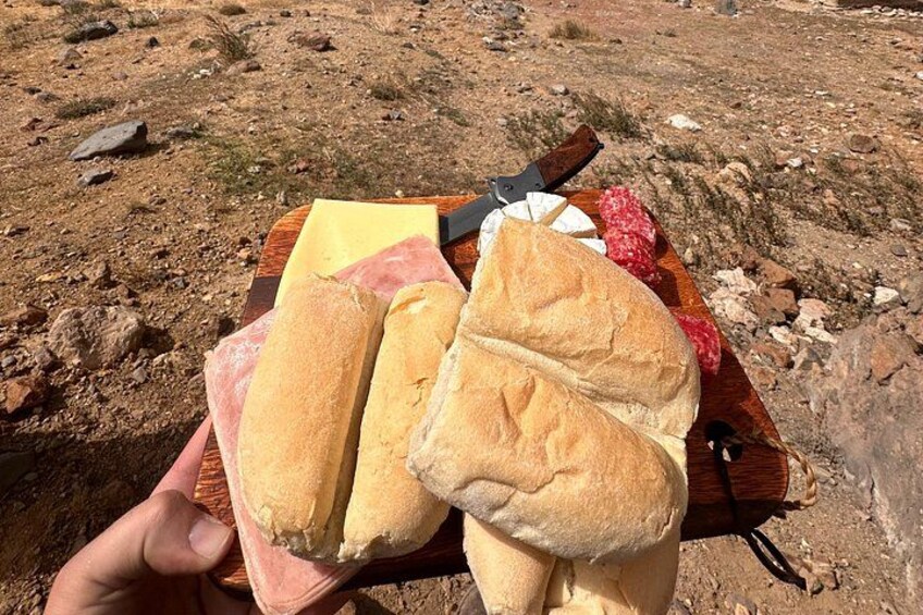 A hand holding a wooden board with bread and cheese. 4
