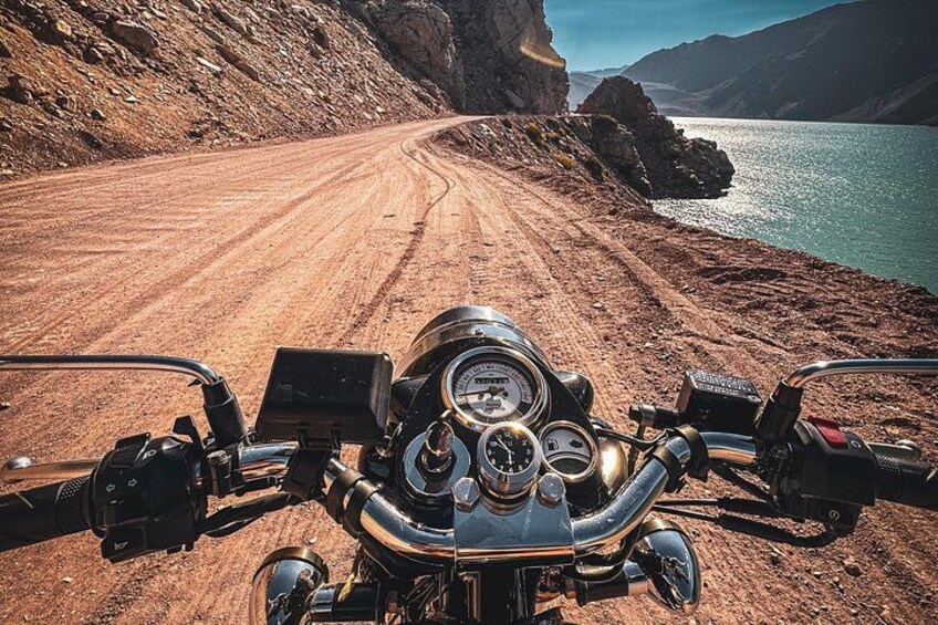 A motorcycle on a dirt road with a body of water and mountains in the background. 1