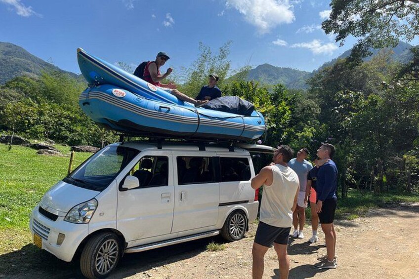 Un fourgon blanc avec un kayak bleu sur le toit, entouré de personnes et dominé par un paysage montagneux. 1