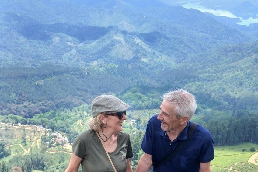 Two people standing on a hill overlooking a valley with a river and mountains in the background. 2