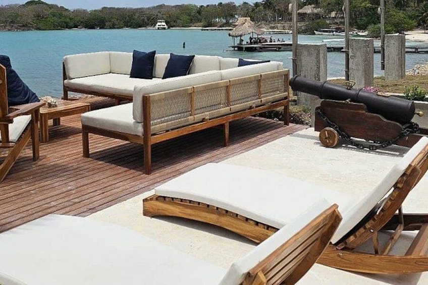 En træterrasse med liggestole og sofa med udsigt over vandet. 2