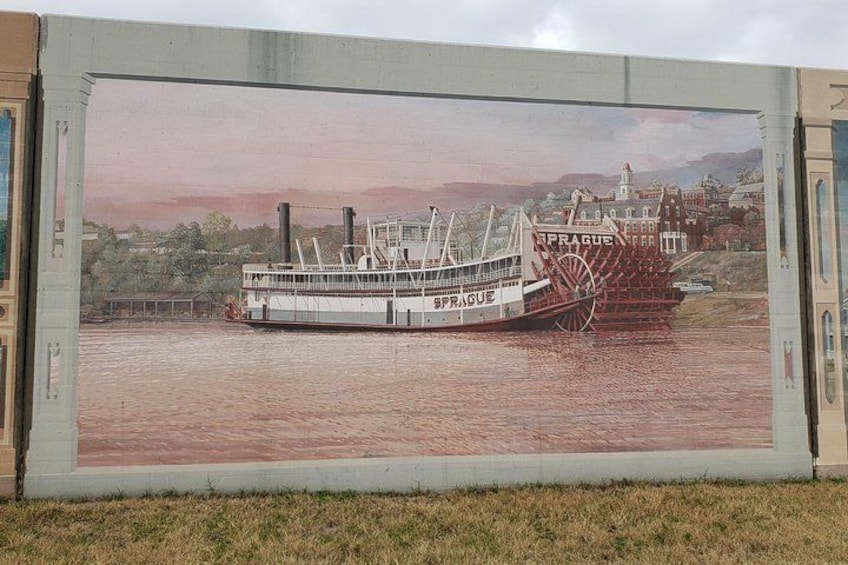 A river scene with a steamboat named 'SPRAGUE' docked at a pier, surrounded by buildings and greenery. 1