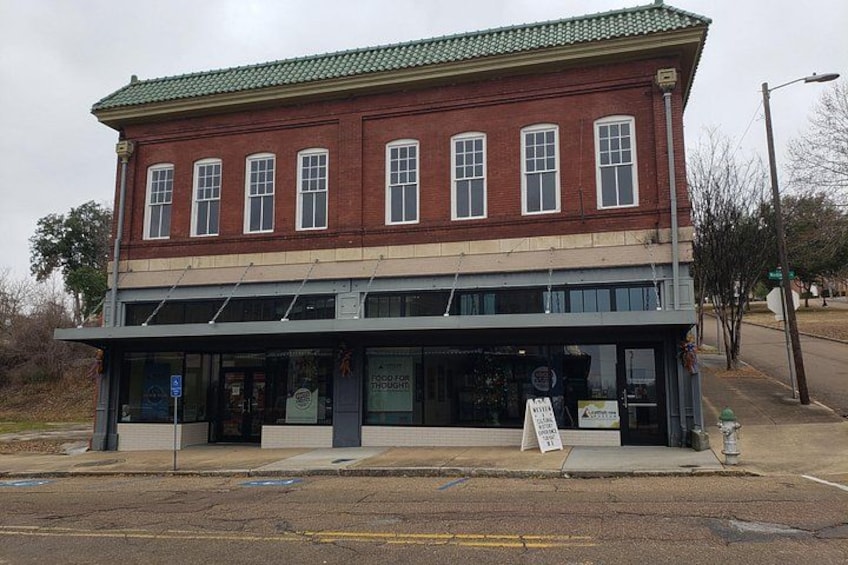 A two-story brick building with a green roof and a storefront. 5
