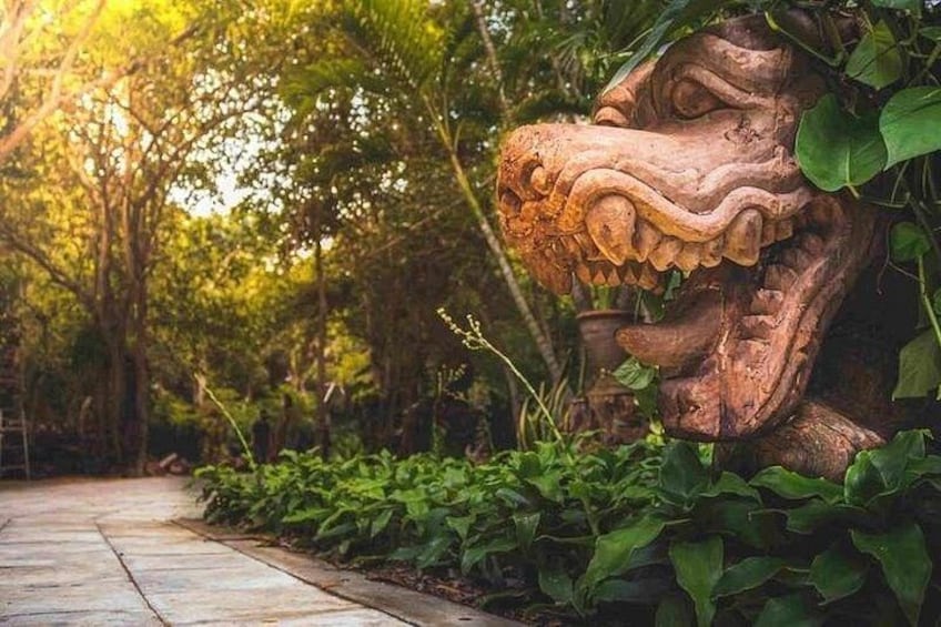 En skulptur föreställande ett lejonhuvud, huggen i sten, står i en trädgård med en stenlagd gång och frodigt grönska. 4