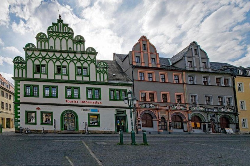 A street with historic buildings, a green and white building with 'Tourist Information' signage, and a cobblestone road. 2