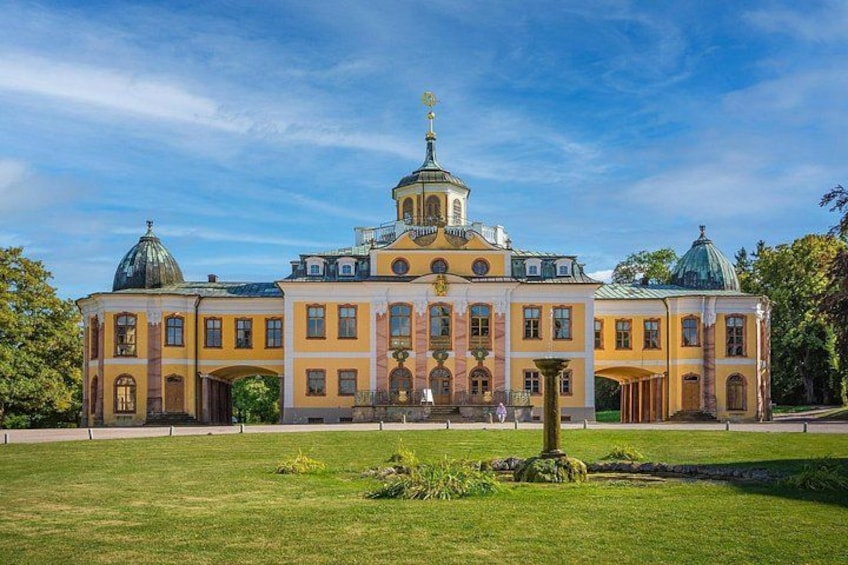 A large, historic building with domed roofs and a central tower, surrounded by a well-maintained lawn and trees. 3