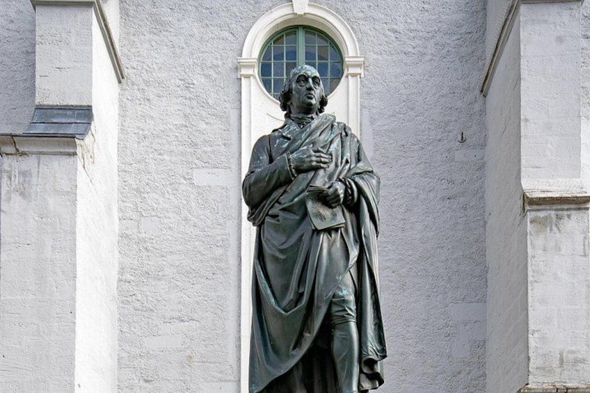 A statue of a man in a robe standing in front of a building with a window. 5