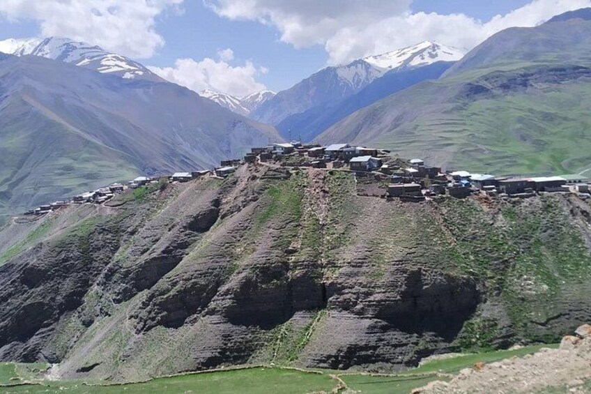 A mountainous landscape with a settlement on a slope, surrounded by snow-capped peaks. 2