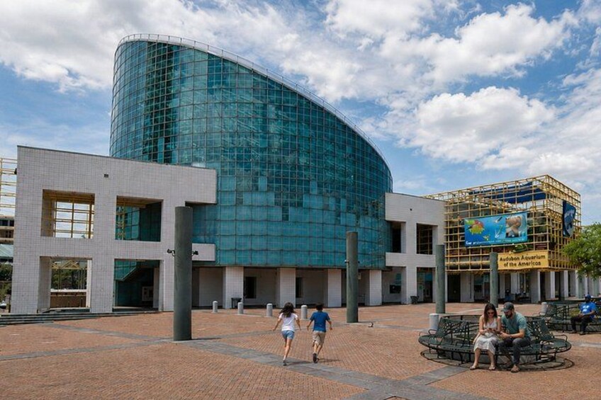 A modern building with a curved glass facade, a brick plaza, and a sign for the Audubon Aquarium of the Americas. 3