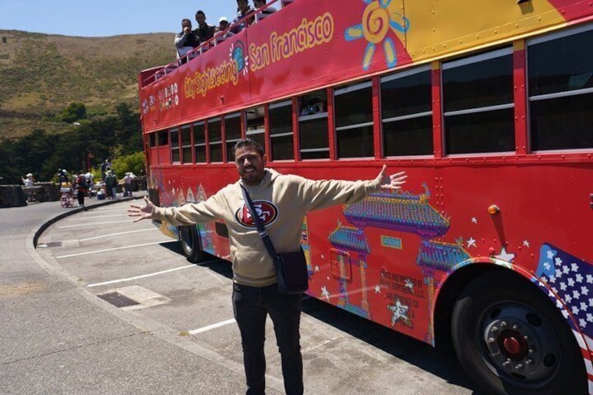 Un autobús rojo de dos pisos con la leyenda 'San Francisco' y 'City Sightseeing', estacionado en una carretera con un paisaje montañoso al fondo. 3