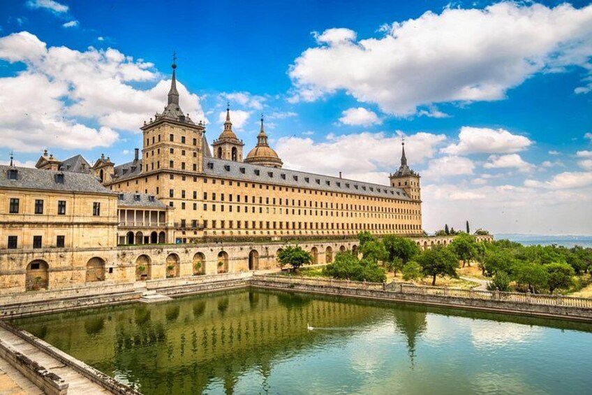 A large historic building with multiple towers, a courtyard, and a reflecting pool. 3