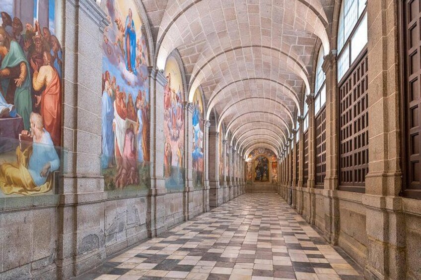 A long corridor with arched ceilings and tiled floors, adorned with colorful frescoes on the walls. 4