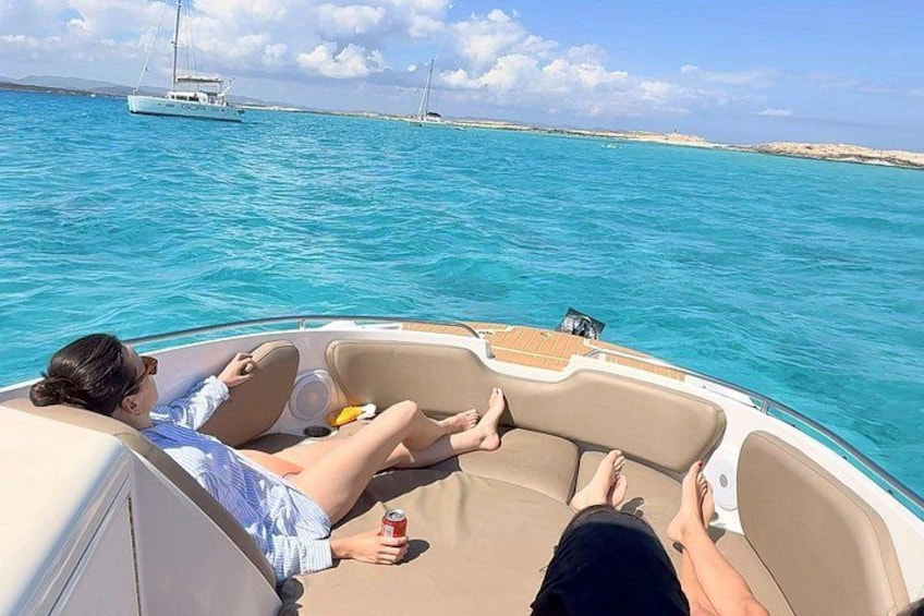 A boat with two people relaxing on the deck, surrounded by turquoise water and distant land. 2
