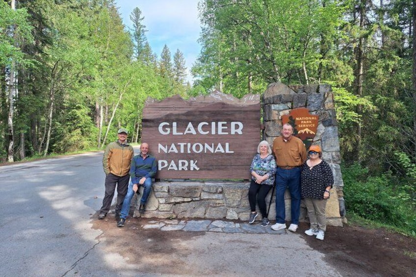 A group of people standing in front of a sign for Glacier National Park. 5