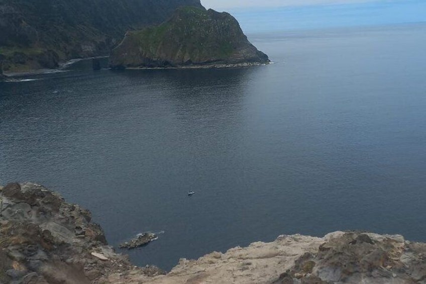 A coastal landscape with a rocky outcrop in the foreground and a calm sea extending to the horizon. 4