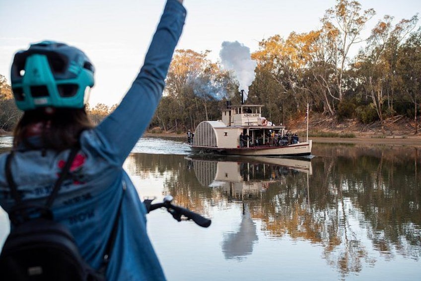 Una persona en bicicleta con casco, un bote con chimenea y árboles reflejados en el agua. 5
