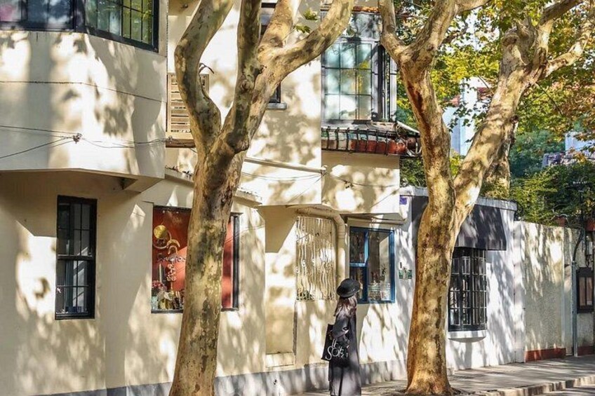 A tree-lined street with buildings, a person walking, and a clear sky. 2