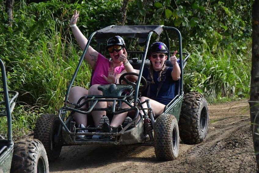 Two people in a four-wheeled off-road vehicle on a dirt path surrounded by greenery. 5