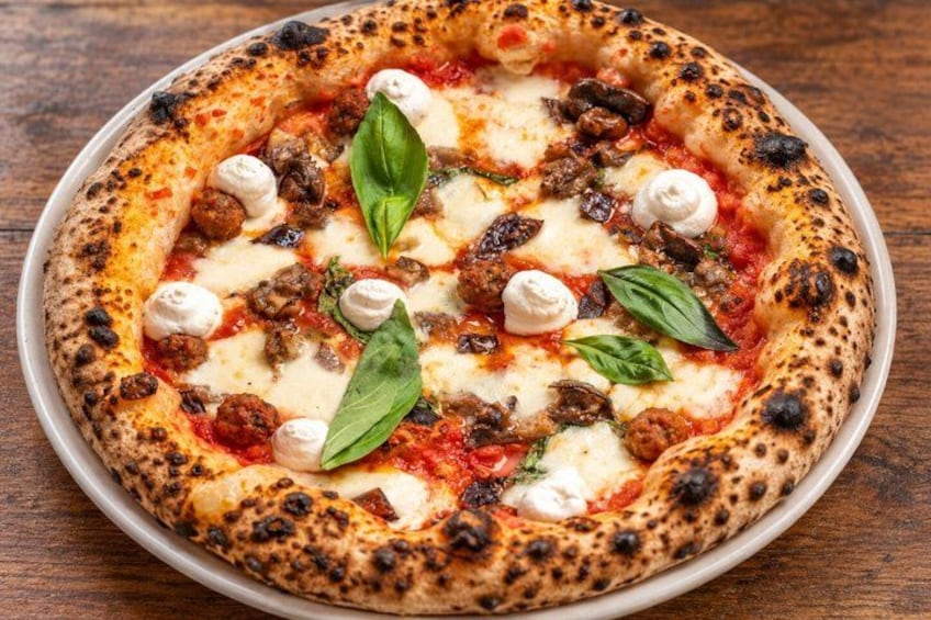 A pizza with toppings and basil leaves on a wooden table. 5