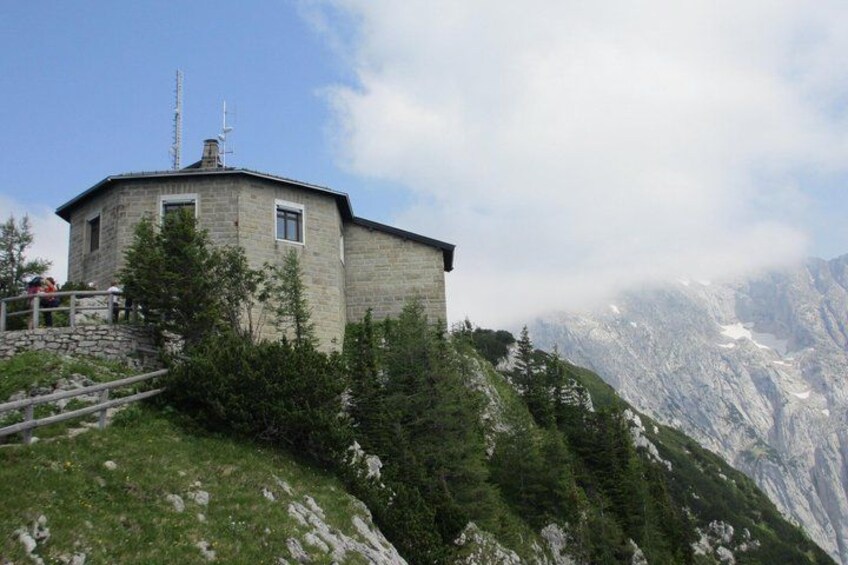 A stone building with a metal antenna, surrounded by trees and mountains. 2