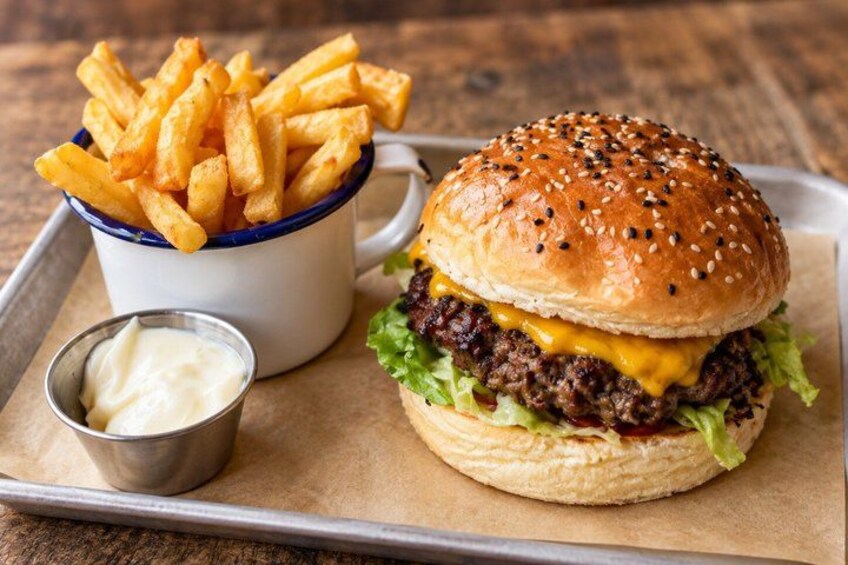 A burger with a sesame seed bun, lettuce, and cheese, accompanied by French fries and a small container of sauce. 4