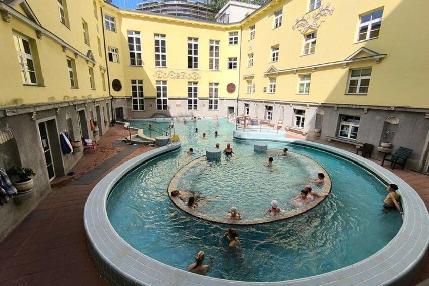 Ein runder Pool, umgeben von gelben Gebäuden, wo Menschen schwimmen und entspannen. 5
