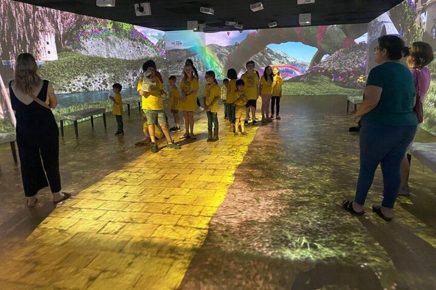 A group of people in yellow shirts standing in a line, observing a large projection on the wall. 4