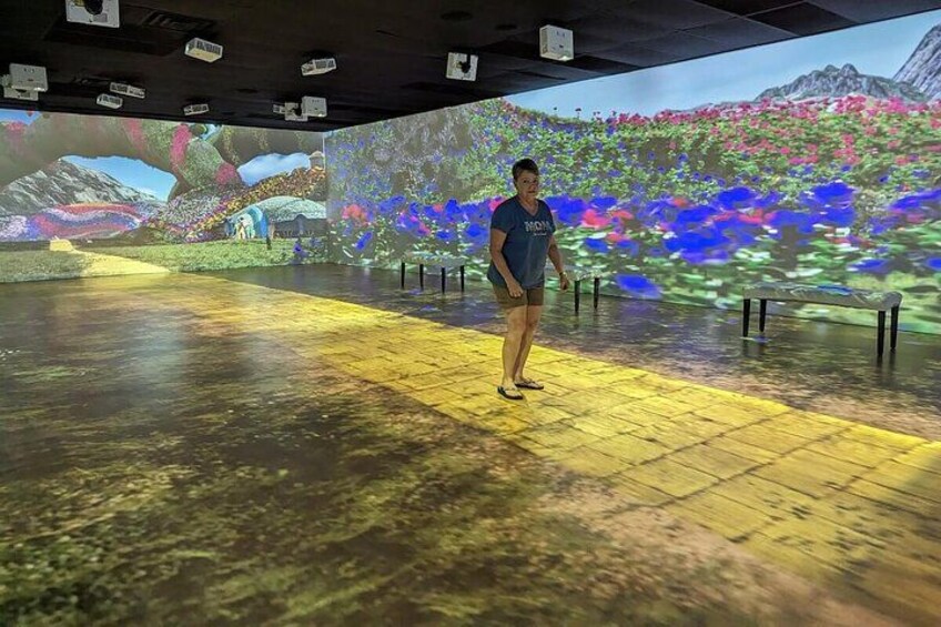 A person standing in a room with a large projection of colorful flowers and a mountainous landscape. 3