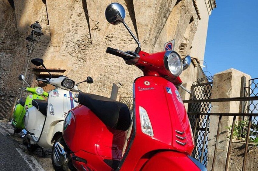 Una scooter roja estacionada frente a un muro de piedra con una reja de metal. 1