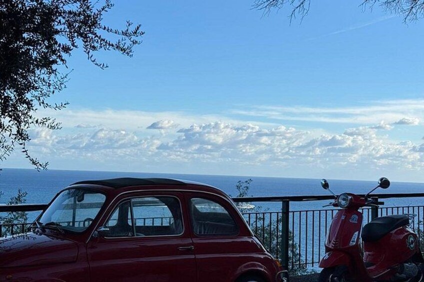 Un coche rojo y un patinete rojo aparcados junto a una barandilla con vistas al mar. 2