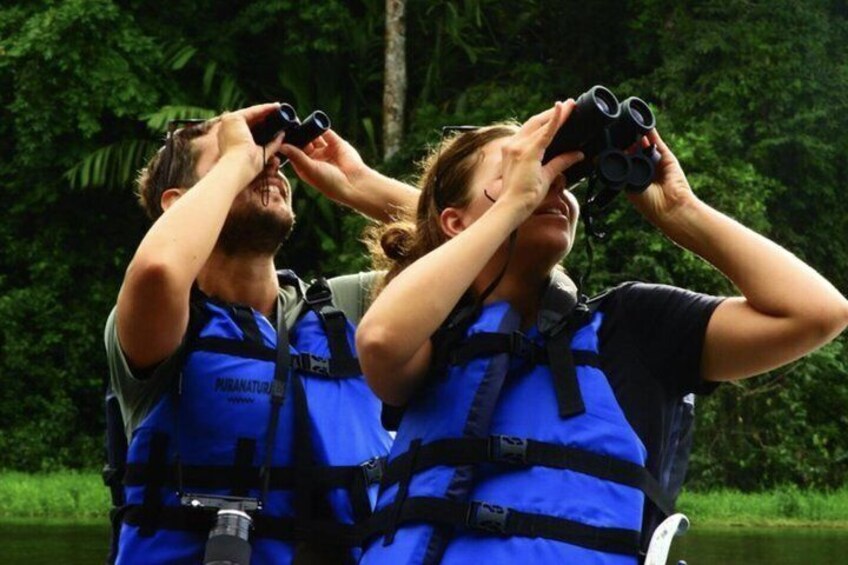 Two people wearing blue life jackets and binoculars, likely engaged in bird watching or nature observation. 5