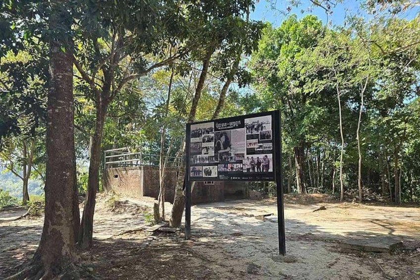 A signboard with historical photos and text in a forested area. 1