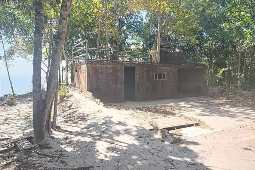 A rustic wooden structure with a metal railing, surrounded by trees and a dirt path. 3