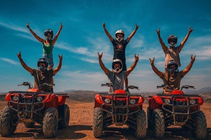 Tres personas en vehículos todo terreno con los brazos levantados en un paisaje desértico. 1