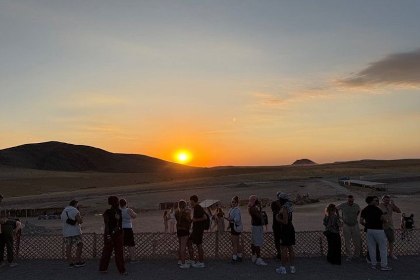 A group of people standing on a flat area, watching the sunset over a desert landscape with hills in the distance. 2