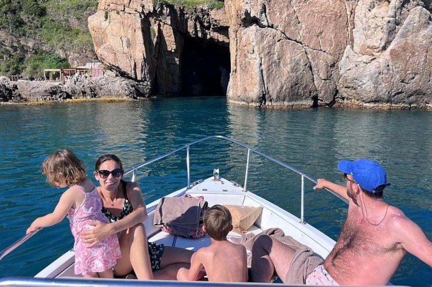 A boat with four people on a calm body of water, rocky cliffs in the background, and a clear sky. 2