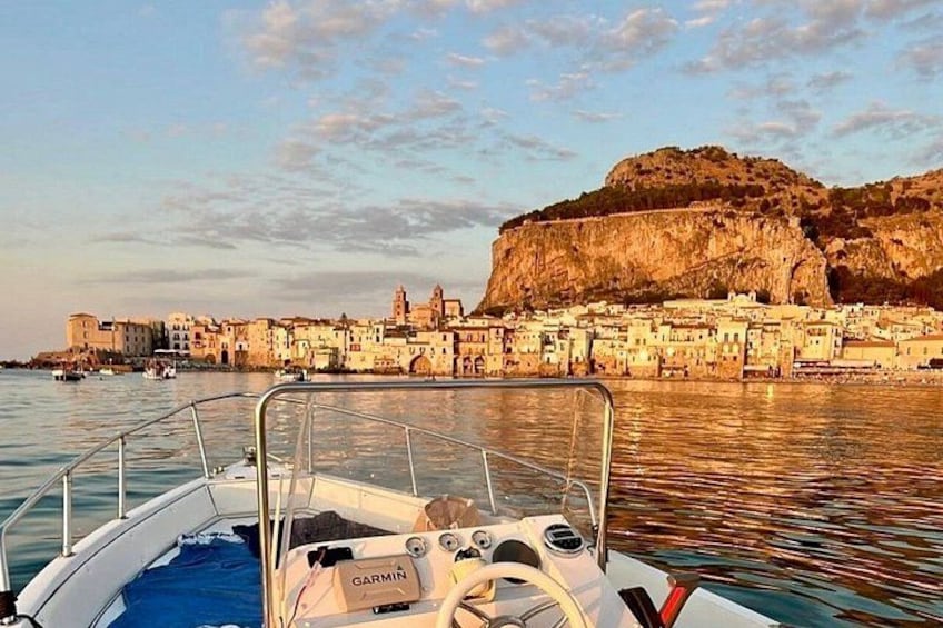 A boat with a Garmin logo, a coastal town with buildings, and a prominent cliff. 1
