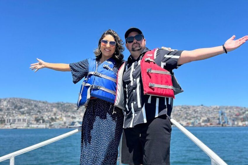 Une personne portant un gilet de sauvetage bleu et une autre portant un gilet de sauvetage rouge se trouvent sur un bateau, avec une vue sur la ville en arrière-plan. 4