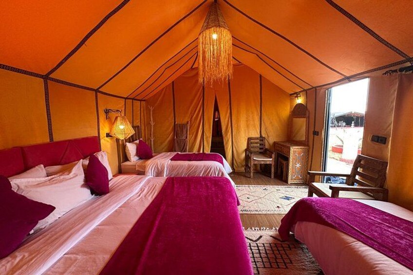 A tent with two beds, a hanging light fixture, and a small table. 3
