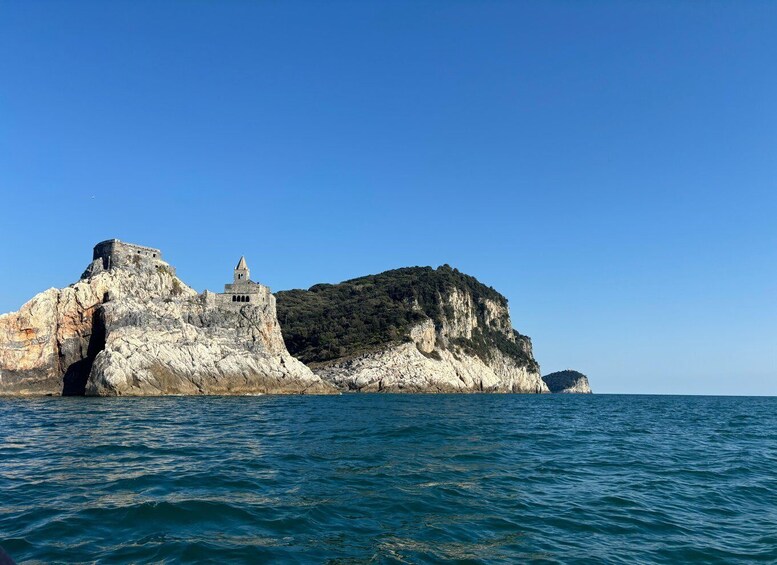 A rocky coastal landscape with a fortified structure on a cliff and a small island in the distance. 3