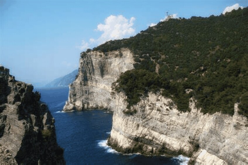 A coastal cliff with a narrow sea passage, surrounded by dense greenery. 1