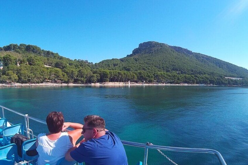 Two people on a boat, a clear blue sea, and a green hill in the background. 3