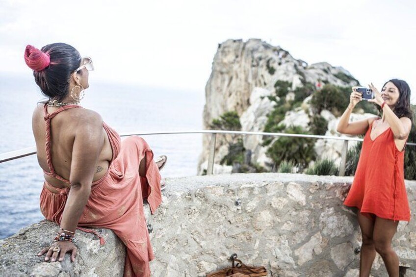 Two people taking a selfie by a rocky seaside with a large rock formation in the background. 2