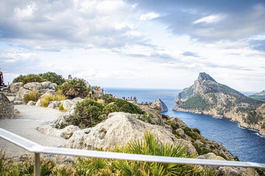 A coastal landscape with rocky terrain, a clear sky, and a distant mountain peak. 1
