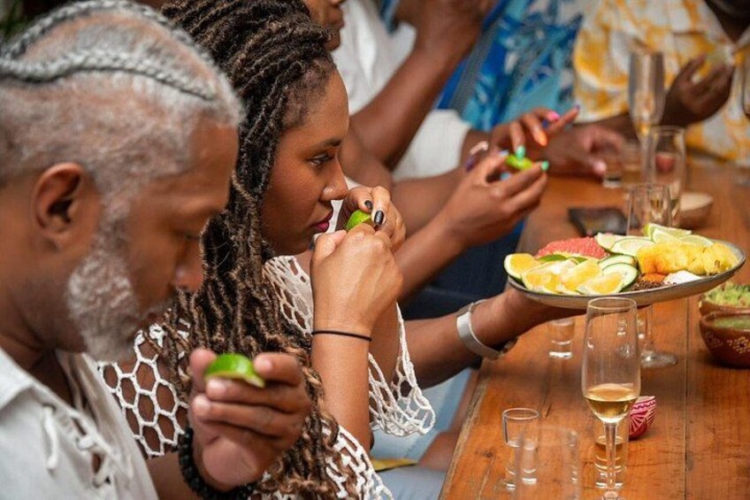 Des personnes sont assises autour d’une table en bois, devant des assiettes remplies de nourriture et des verres contenant un liquide clair, peut-être du vin. 5