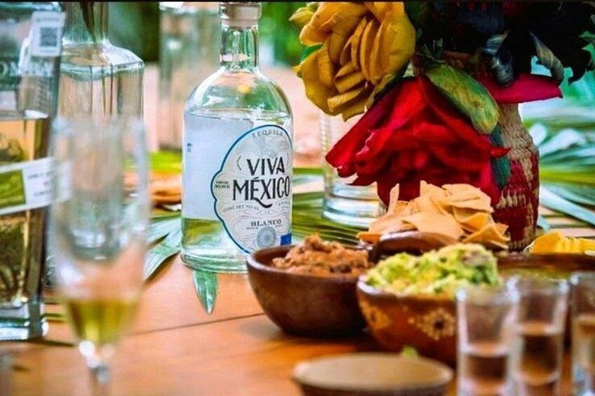 Une bouteille de tequila Viva Mexico, un bol de guacamole et un vase rempli de fleurs sur une table. 3