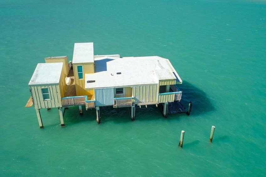 A floating house with multiple levels and a dock extending into turquoise water. 4
